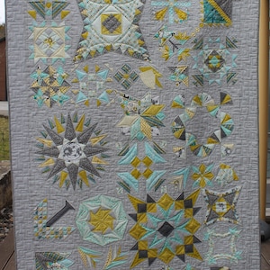 Könnte beinhalten: Eine Decke mit grauem Hintergrund und einer Vielzahl geometrischer Muster in den Farben Türkis, Gelb und Grau. Die Decke besteht aus vielen verschiedenen Blöcken, die jeweils ein einzigartiges Design haben.