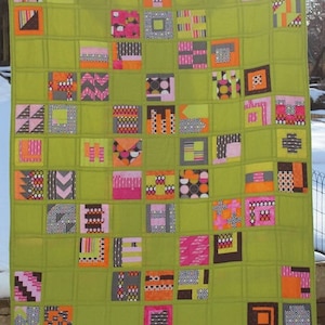 Może przedstawiać: Zielona kołdra w patchworku z kwadratami w różnych kolorach i wzorach, w tym różowym, pomarańczowym, czarnym i białym.