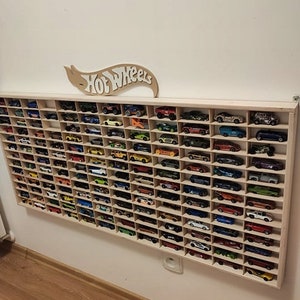 May include: A wooden wall-mounted display shelf with a Hot Wheels logo above it. The shelf is filled with rows of colorful toy cars.