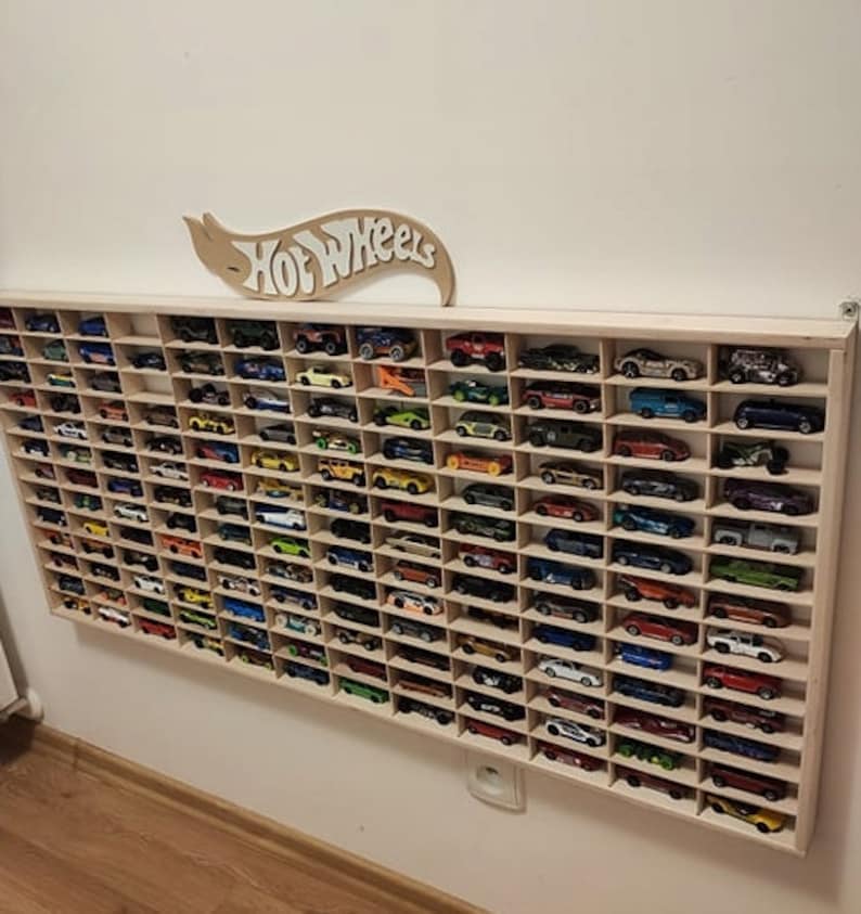 May include: A wooden wall-mounted display shelf with a Hot Wheels logo above it. The shelf is filled with rows of colorful toy cars.