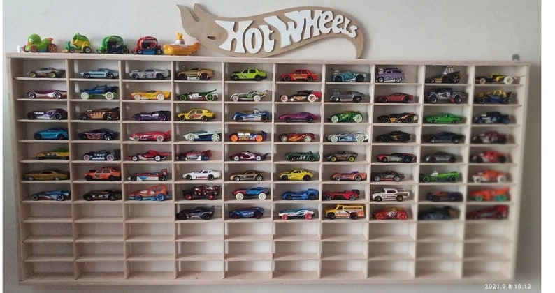 May include: A wooden shelf unit with 72 individual slots for displaying Hot Wheels toy cars. The shelf is filled with a variety of colorful toy cars.