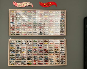 May include: Two wooden display cases with glass fronts filled with a collection of Hot Wheels toy cars. The cases are mounted on a wall and labeled "Hot Wheels" and "Kiko".
