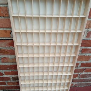 May include: A wooden display case with a grid of small compartments. The case is made of light wood and has a natural finish.