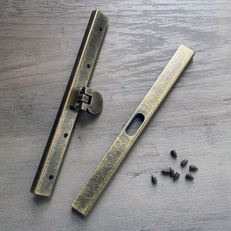 May include: Two antique gold metal clasps with a hinge and small holes for screws. The clasps are on a wooden surface with small black screws scattered around them.