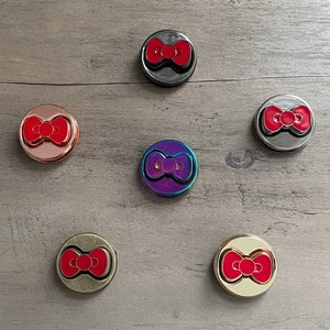 Op de afbeelding: Zes ronde, metalen, decoratieve telefoonbeugels met een rood strikdesign. De beugels zijn in verschillende kleuren, waaronder zwart, zilver, goud, rosé goud en iriserend.