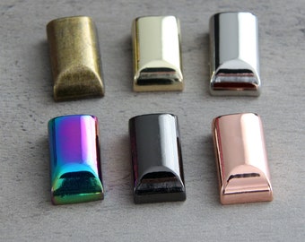 May include: Six rectangular metal end caps in various finishes: antique brass, gold, silver, iridescent, black, and rose gold. Each cap has a rounded bottom edge and a polished, reflective surface, ideal for crafting or jewelry making.
