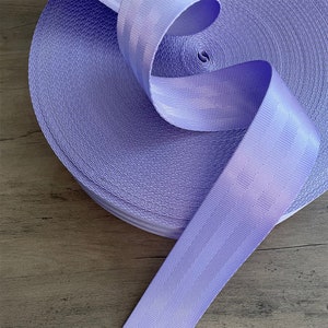 May include: A roll of lavender purple webbing with white stripes. The webbing is rolled up and the end is hanging down.