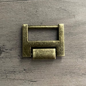 May include: A gold-toned metal buckle with a rectangular shape and a sliding bar. The buckle has a worn, antique finish.
