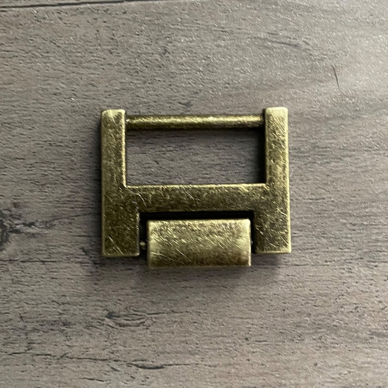 May include: A gold-toned metal buckle with a rectangular shape and a sliding bar. The buckle has a worn, antique finish.