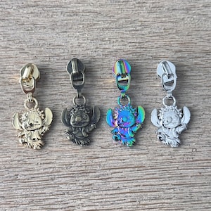 May include: Four metal zipper pulls featuring a cartoon character in gold, gunmetal, iridescent, and silver finishes. Each pull has a detailed design of the character with large ears and a smiling expression. The pulls are attached to metal zipper slides.