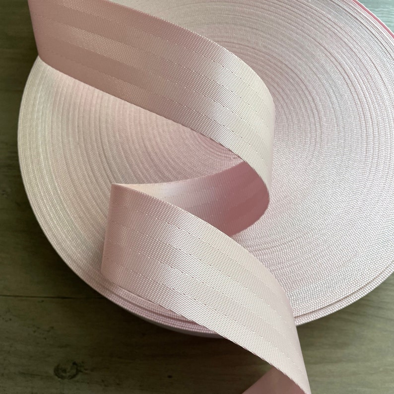 May include: A roll of pink webbing with a textured surface. The webbing is rolled up and the end is hanging down.
