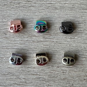 Può includere: Sei fermagli a scatto in metallo di diversi colori. I fermagli sono di forma ovale con due fori su ciascun lato. I colori sono oro rosa, iridescente, nero, argento, oro e ottone anticato.