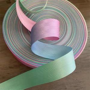 May include: Three rolls of pastel colored webbing, in shades of green, blue, and pink. The webbing is woven with a subtle texture and has a slight sheen.
