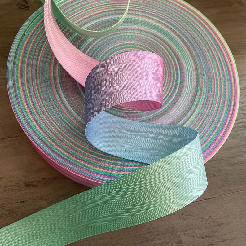 May include: Three rolls of pastel colored webbing, in shades of green, blue, and pink. The webbing is woven with a subtle texture and has a slight sheen.