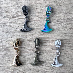 May include: Five zipper pulls with witch hat charms in various metallic finishes. The zipper pulls include black, iridescent, gold, bronze, and silver. The witch hat charms are attached to the zipper pulls with a small ring.