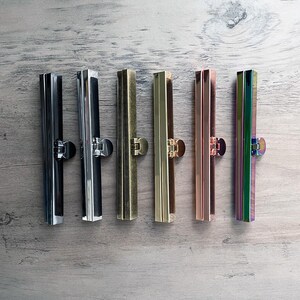 May include: Six metal purse frame clasps in different finishes: black, silver, brass, gold, rose gold, and iridescent.