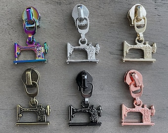 Pode incluir: Seis puxadores de zíper de metal de diferentes cores com um design de máquina de costura. Os puxadores de zíper são nas cores arco-íris, prata, ouro, preto e ouro rosa.