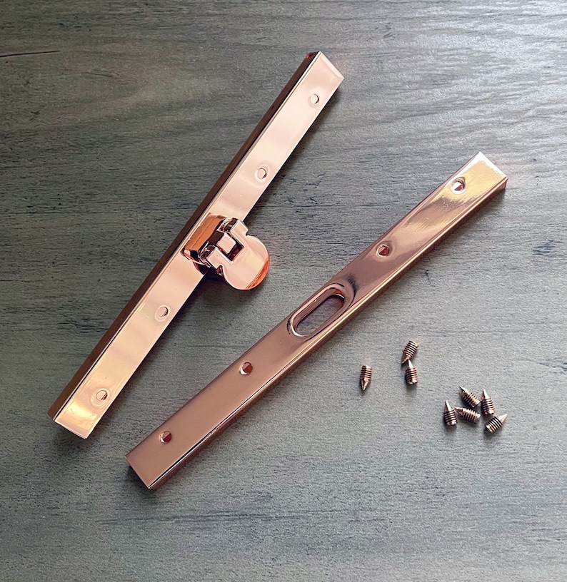 May include: Two rose gold metal purse frame pieces with a rose gold metal clasp and eight small rose gold screws.