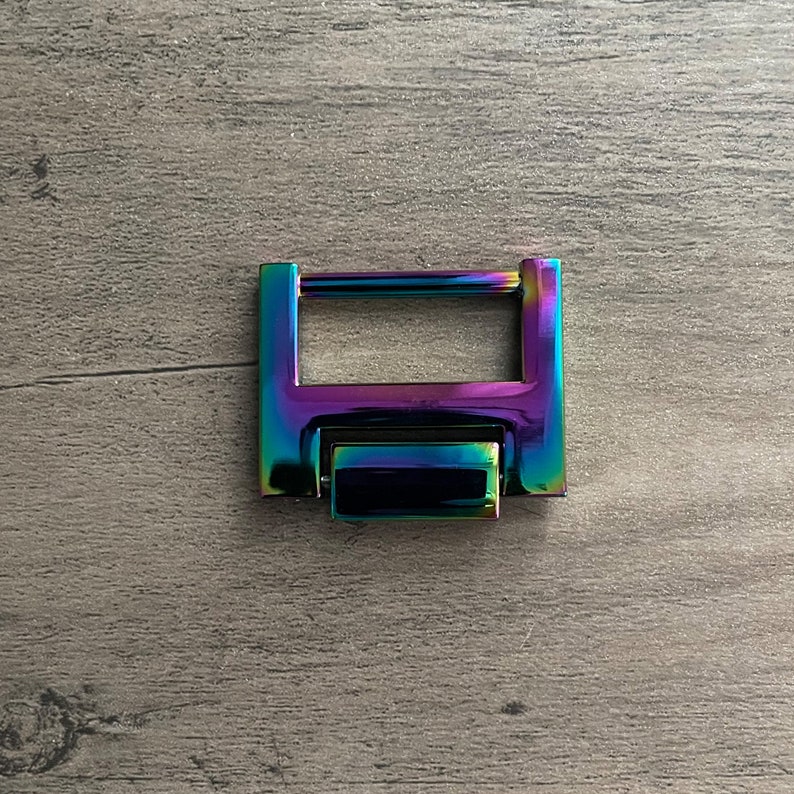 May include: A rainbow iridescent metal buckle with a rectangular shape and a sliding latch. The buckle is made of metal and has a shiny finish.