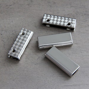 May include: Four silver metal slider buckles with a geometric pattern. The buckles are rectangular and have two holes on each side.