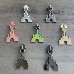 May include: Seven zipper pulls in different colors, each featuring a detailed castle design. The colors include silver, gold, rose gold, black, rainbow, and two shades of bronze.