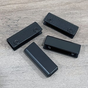 May include: Four black metal glass shelf brackets. Two of the brackets have a textured surface and two are smooth. The brackets are designed to hold glass shelves.