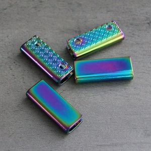 May include: Four iridescent metal slider buckles. The buckles are rectangular and have a textured surface. They are a mix of blue, green, purple, and gold.