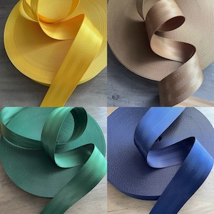 May include: Four spools of webbing in various colors: bright yellow, tan, deep green, and navy blue. Each spool is tightly wound, with a length of the webbing unwound to show its texture and color. The webbing has a subtle ribbed pattern.