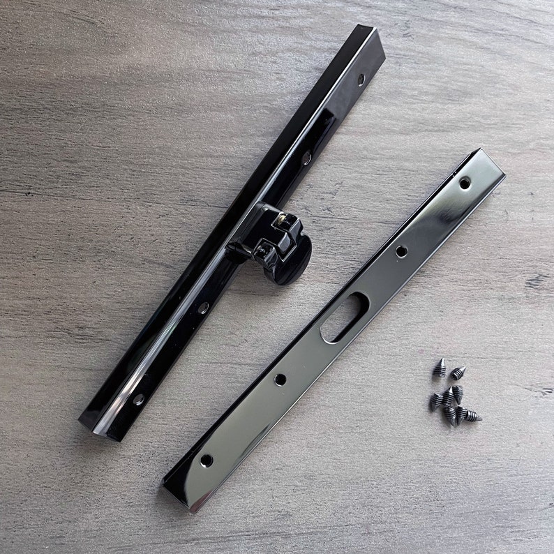 May include: Two black metal brackets with multiple holes and a small black plastic piece with a metal spring. A pile of small black screws are on a wood surface.