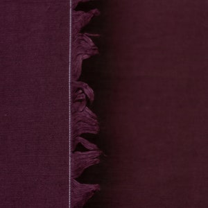 Puede incluir: Primer plano de una tela de color burdeos oscuro con un borde de flecos. La tela tiene una textura sutil y un color intenso.