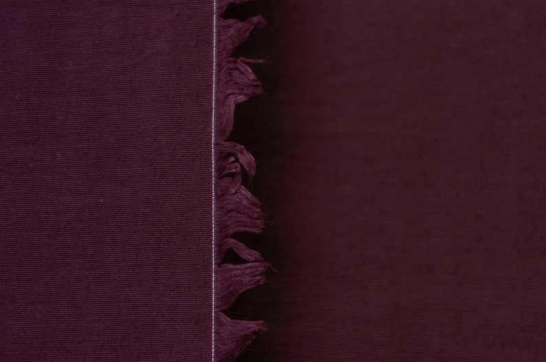 Puede incluir: Primer plano de una tela de color burdeos oscuro con un borde de flecos. La tela tiene una textura sutil y un color intenso.
