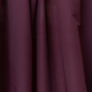 Puede incluir: Un primer plano de una tela de color morado oscuro con una textura suave y sedosa. La tela est&aacute; doblada de forma que crea l&iacute;neas suaves y fluidas.