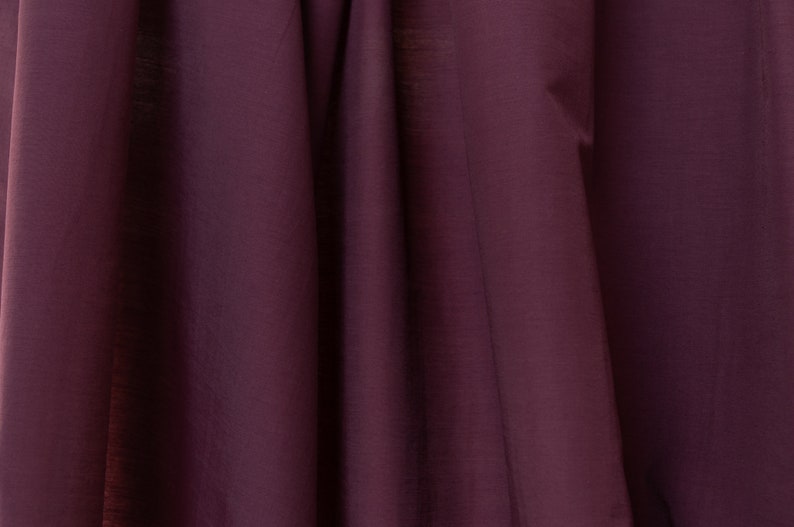 Puede incluir: Un primer plano de una tela de color morado oscuro con una textura suave y sedosa. La tela est&aacute; doblada de forma que crea l&iacute;neas suaves y fluidas.