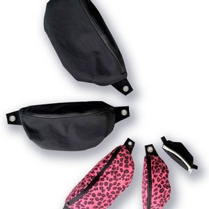 May include: Four fanny packs in different sizes and patterns. Two are black with silver hardware and zippers. Two are pink with a leopard print and silver hardware and zippers.