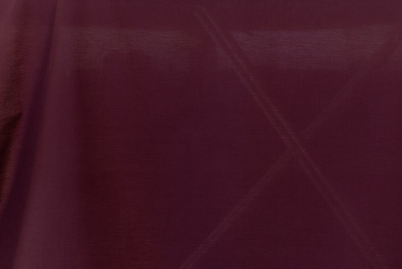Puede incluir: Primer plano de una tela de color burdeos oscuro con una textura suave y sedosa. La tela tiene un brillo sutil y est&aacute; drapeada de forma que crea pliegues y sombras suaves.