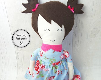 May include: A handmade doll with brown hair, a pink collar, and a blue dress with a floral pattern. The doll is sitting on a white wooden surface. Sewing Pattern.