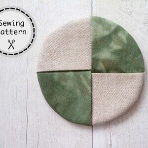 Pu&ograve; includere: Un sottobicchiere rotondo in tessuto verde e beige con un design a patchwork. Il sottobicchiere &egrave; composto da quattro quadrati di tessuto, due verdi e due beige. Il tessuto verde ha un motivo tie-dye.