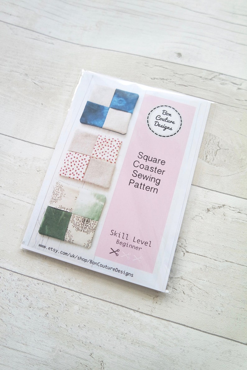 May include: A pink and white card with a sewing pattern for square coasters. The card shows three different designs for the coasters, each with a different fabric pattern. The card also includes the text "Square Coaster Sewing Pattern" and "Skill Level Beginner".