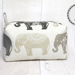 May include: A beige and gray fabric makeup bag with a zipper closure and a black handle. The bag is decorated with a repeating pattern of elephants.