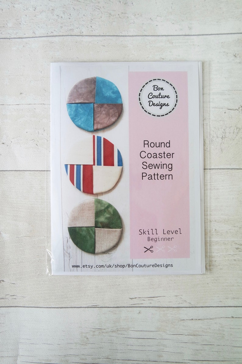 Pu&ograve; includere: Un modello di cucito per un sottobicchiere rotondo. Il modello presenta tre diversi design con uno schema di colori blu, rosso e verde. Il modello &egrave; etichettato come "Round Coaster Sewing Pattern" e "Skill Level Beginner".