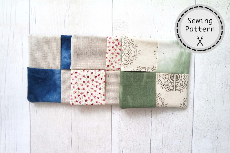 May include: A patchwork quilt block made of nine squares of fabric in various colors and patterns, including beige, blue, green, and white. The fabric squares are sewn together to create a geometric design.