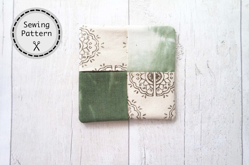 May include: A green and white patchwork fabric coaster with a mandala pattern. The coaster is made of four squares of fabric sewn together.