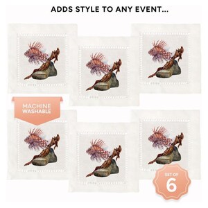 May include: Set of six white linen cocktail napkins with a red and orange lionfish design. The napkins feature a machine washable label. "Set of 6" is printed on the bottom right corner of the image.