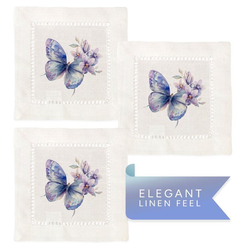 K&ouml;nnte beinhalten: Set aus drei wei&szlig;en Leinen-Servietten mit einer zarten, gestickten Bord&uuml;re. Jede Serviette zeigt eine Aquarell-Illustration eines lilafarbenen Schmetterlings mit Blumen.