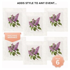 May include: Set of six white linen cocktail napkins with a purple lilac floral design. The napkins are machine washable and have a delicate embroidered border. "Set of 6" is printed on a peach-colored circle.