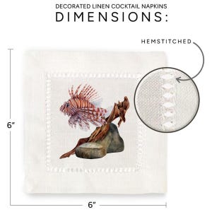 May include: White linen cocktail napkin with a hemstitched border. The napkin features a watercolor illustration of a lionfish on a piece of driftwood. The napkin measures 6 inches by 6 inches.
