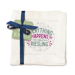 May include: A square white linen napkin set tied with a navy blue ribbon and a green tag. The napkin features the text "Everything Happens for a Riesling" in a circular design with wine-related illustrations.