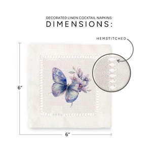 K&ouml;nnte beinhalten: Wei&szlig;e Cocktail-Serviette aus Leinen mit einem Saum. Die Serviette zeigt eine Aquarell-Illustration eines blauen Schmetterlings mit lila Blumen. Die Serviette misst 15,24 cm x 15,24 cm.