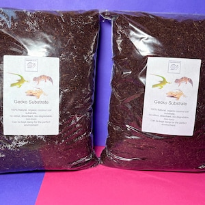 May include: Two clear plastic bags filled with brown organic coconut coir substrate for reptiles. The bags have labels that say "Gecko Substrate" and include information about the product. The labels also feature images of geckos.