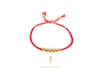 Pode incluir: Um bracelete de cordão vermelho com contas douradas. O bracelete é ajustável e tem um design simples.